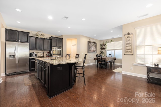 kitchen featuring sink, a breakfast bar area, dark wood-type flooring, stainless steel appliances, and an island with sink