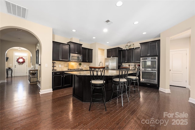 kitchen featuring a breakfast bar, stainless steel appliances, light stone countertops, an island with sink, and decorative backsplash