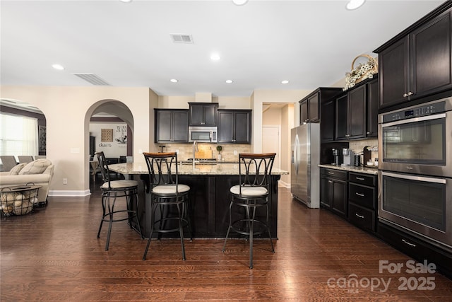 kitchen with stainless steel appliances, light stone countertops, a kitchen island with sink, and a kitchen breakfast bar