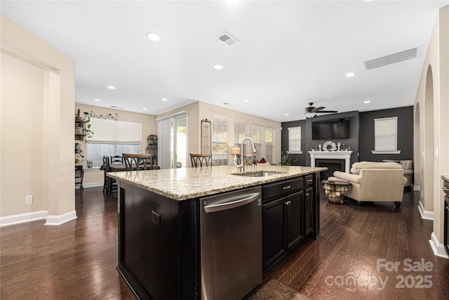 kitchen featuring sink, dishwasher, dark hardwood / wood-style floors, light stone counters, and an island with sink