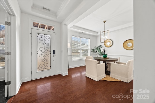 foyer with dark wood-type flooring, ornamental molding, a raised ceiling, and a chandelier