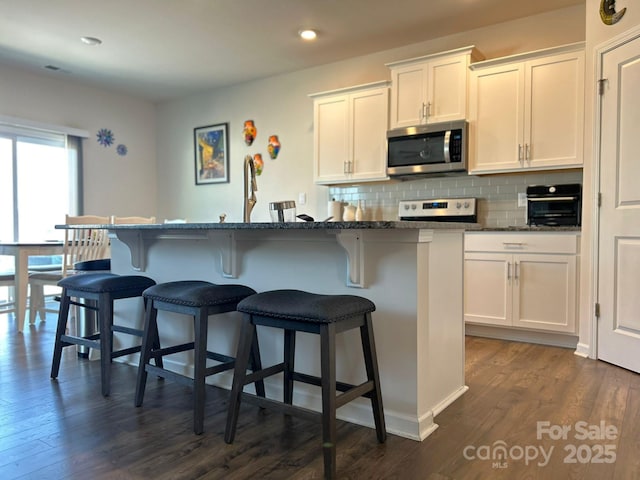 kitchen featuring white cabinetry, appliances with stainless steel finishes, a kitchen island with sink, and dark stone countertops