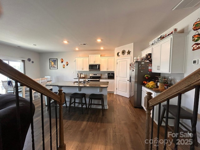 kitchen featuring a breakfast bar, white cabinetry, dark hardwood / wood-style floors, stainless steel appliances, and a kitchen island with sink