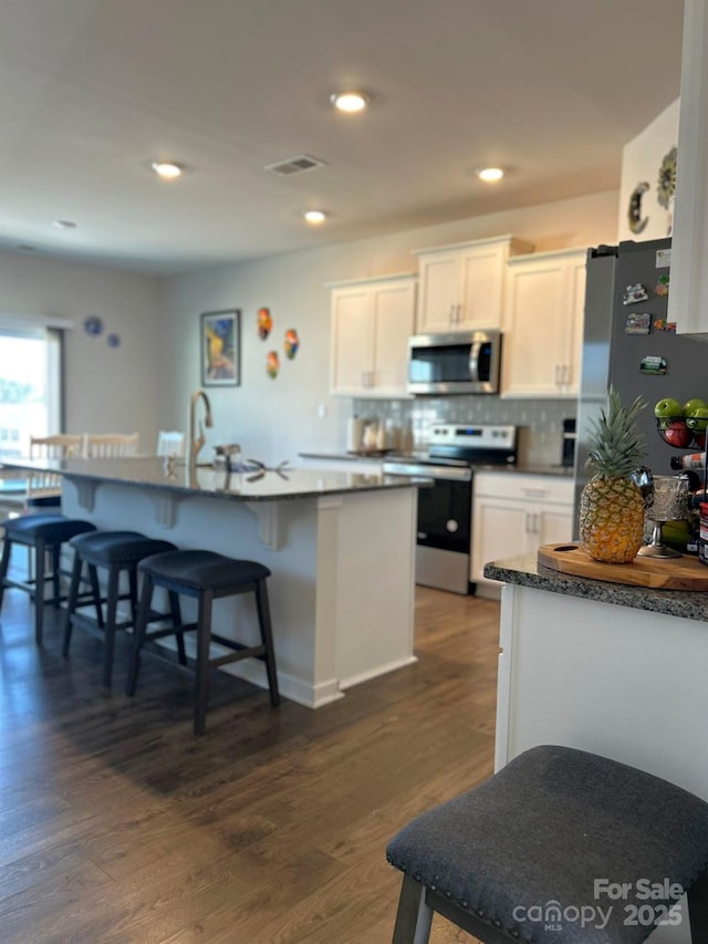 kitchen with white cabinets, a kitchen breakfast bar, decorative backsplash, stainless steel appliances, and dark wood-type flooring