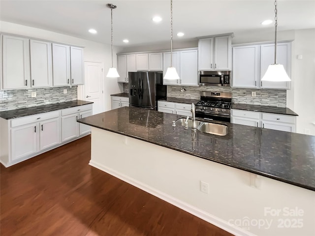 kitchen featuring white cabinets, appliances with stainless steel finishes, hanging light fixtures, and dark stone counters