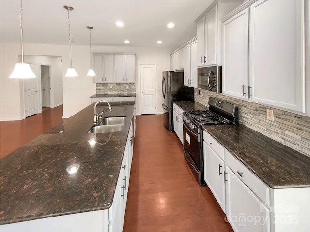 kitchen featuring pendant lighting, sink, appliances with stainless steel finishes, white cabinets, and a center island with sink