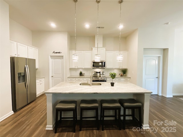 kitchen featuring white cabinetry, appliances with stainless steel finishes, an island with sink, and hanging light fixtures