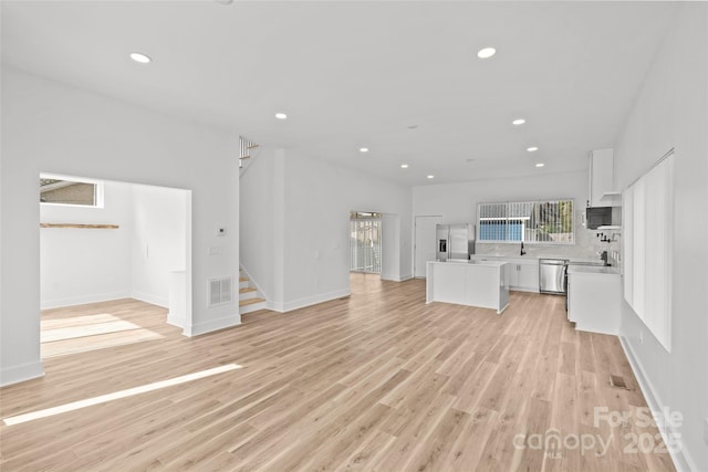 unfurnished living room featuring recessed lighting, visible vents, baseboards, light wood-style floors, and stairway