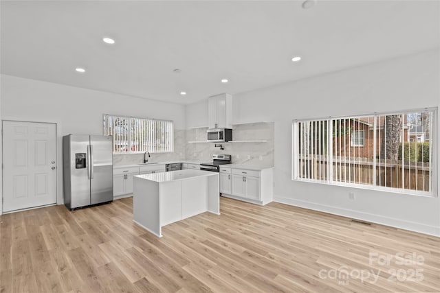 kitchen with light wood finished floors, stainless steel appliances, light countertops, white cabinetry, and a sink