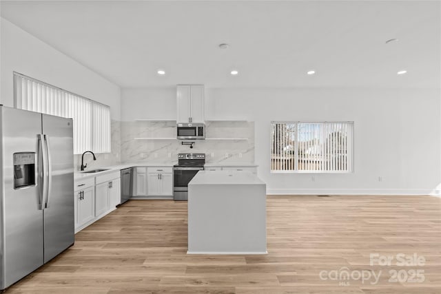 kitchen with stainless steel appliances, a sink, white cabinetry, light wood-style floors, and light countertops