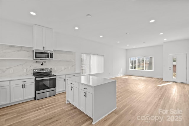 kitchen featuring stainless steel appliances, light wood-type flooring, white cabinetry, and backsplash