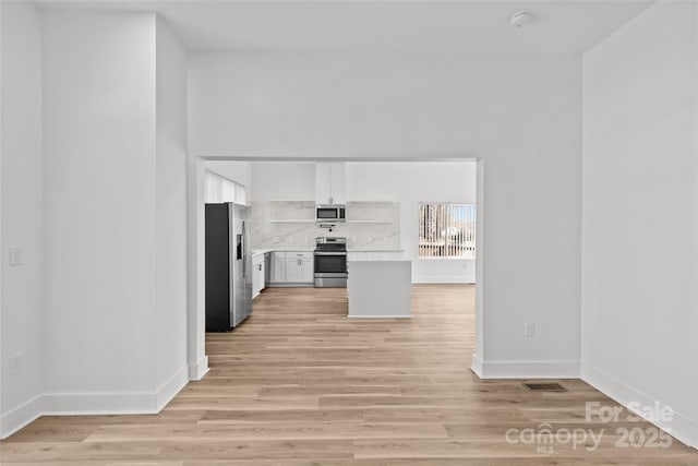 kitchen featuring white cabinets, light countertops, appliances with stainless steel finishes, decorative backsplash, and light wood finished floors