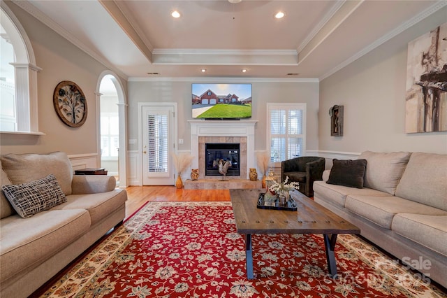 living room with a fireplace, ornamental molding, a raised ceiling, and light wood-type flooring