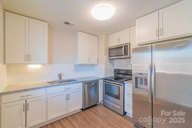 kitchen with sink, light hardwood / wood-style flooring, appliances with stainless steel finishes, light stone counters, and white cabinets