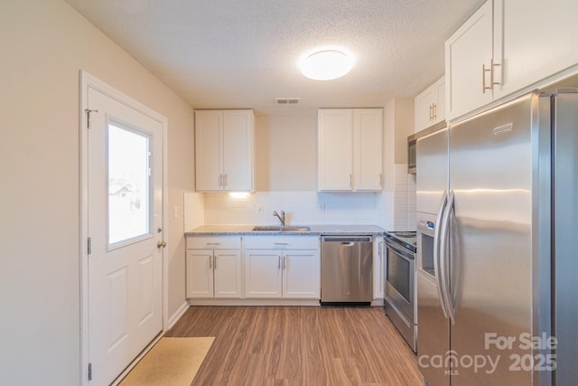 kitchen featuring stainless steel appliances, white cabinetry, light stone countertops, and sink