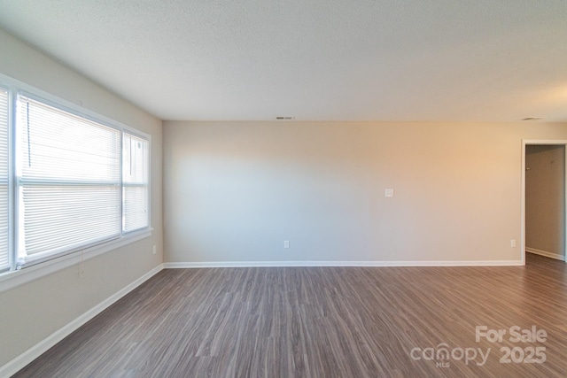 empty room with dark wood-type flooring and a textured ceiling