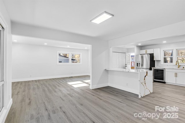 kitchen with stainless steel refrigerator with ice dispenser, wine cooler, a breakfast bar area, white cabinetry, and kitchen peninsula