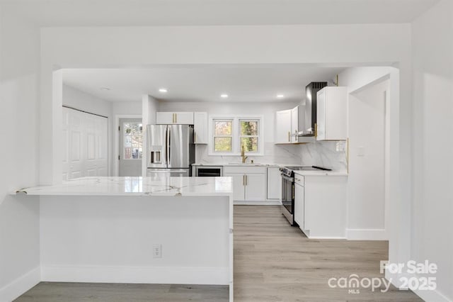 kitchen with sink, white cabinets, kitchen peninsula, stainless steel appliances, and wall chimney range hood