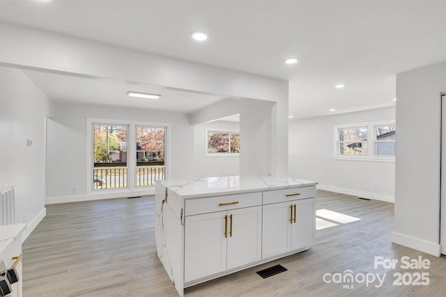 kitchen with a healthy amount of sunlight, light stone countertops, light hardwood / wood-style floors, and white cabinets