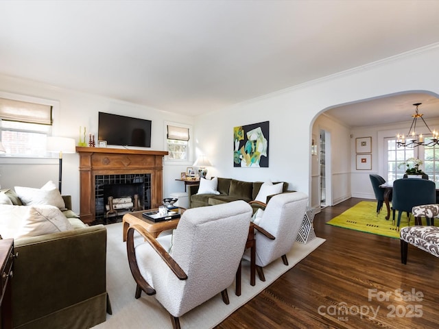 living room with dark hardwood / wood-style flooring, crown molding, a chandelier, and a tiled fireplace