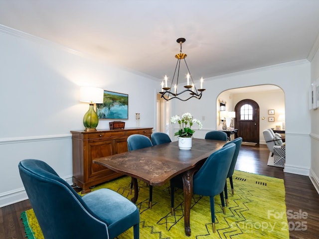 dining area with dark wood-type flooring, crown molding, and an inviting chandelier