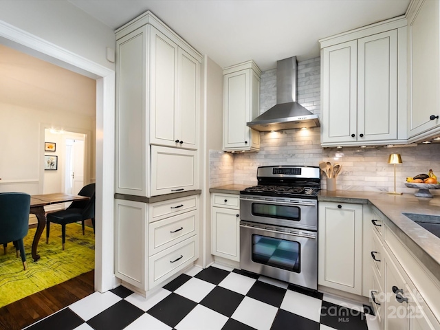 kitchen featuring wall chimney range hood, backsplash, double oven range, and white cabinets