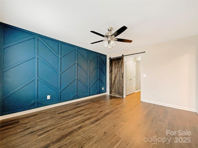 spare room featuring a barn door, hardwood / wood-style floors, and ceiling fan