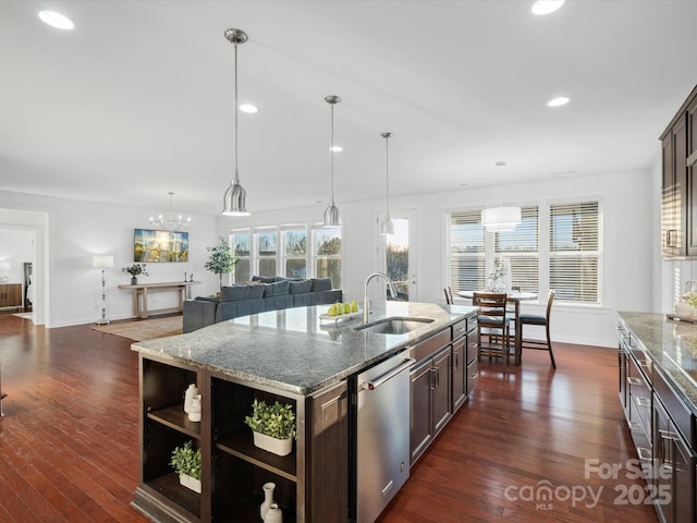 kitchen featuring an island with sink, dishwasher, sink, light stone countertops, and dark brown cabinets