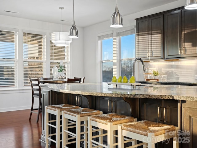 kitchen featuring hanging light fixtures, dark brown cabinets, light stone counters, and decorative backsplash