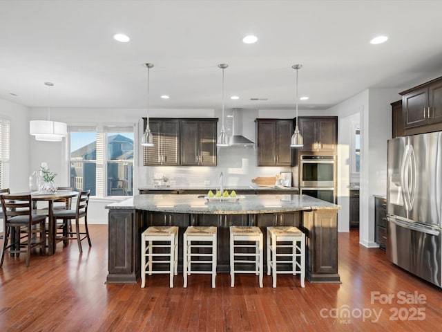 kitchen featuring a kitchen island, appliances with stainless steel finishes, pendant lighting, and wall chimney range hood