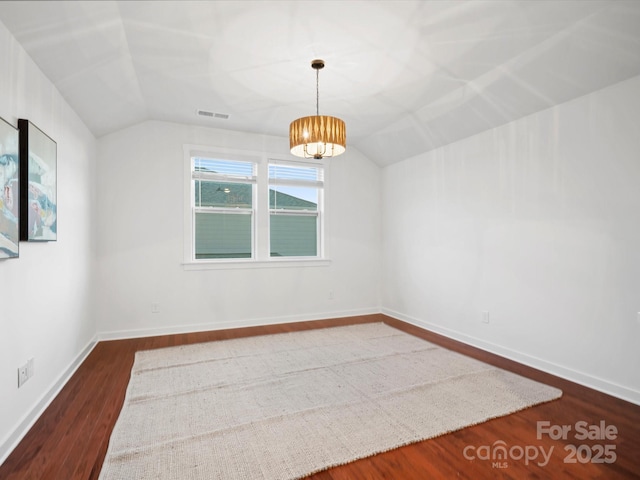 empty room featuring dark wood-type flooring, vaulted ceiling, and a notable chandelier