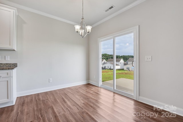 unfurnished dining area featuring hardwood / wood-style flooring, ornamental molding, and an inviting chandelier