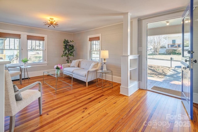 living area with ornamental molding, light wood-type flooring, and baseboards