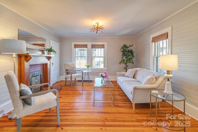 living area featuring ornamental molding, a fireplace, light wood-style flooring, and baseboards