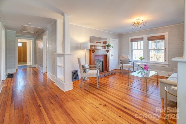 living room featuring a fireplace with raised hearth, visible vents, ornamental molding, hardwood / wood-style floors, and decorative columns