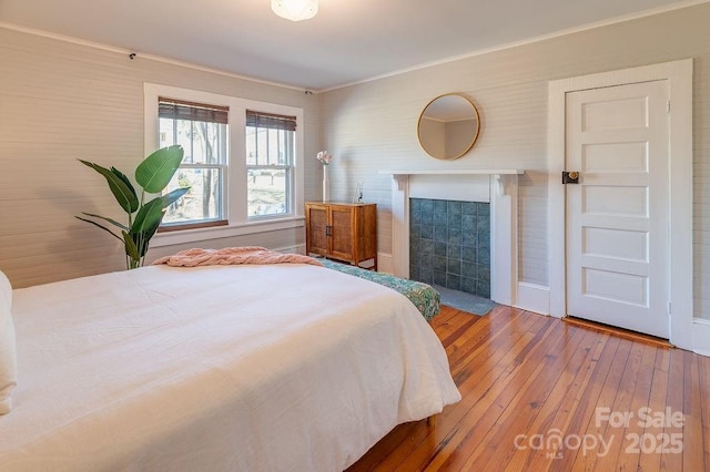 bedroom with ornamental molding, a tile fireplace, and wood-type flooring