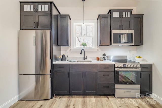 kitchen featuring light countertops, hanging light fixtures, appliances with stainless steel finishes, a sink, and light wood-type flooring