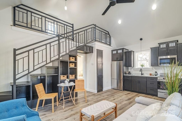 living area featuring light wood finished floors, baseboards, a ceiling fan, stairs, and high vaulted ceiling