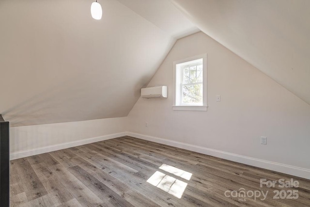 additional living space featuring wood finished floors, vaulted ceiling, baseboards, and a wall mounted AC