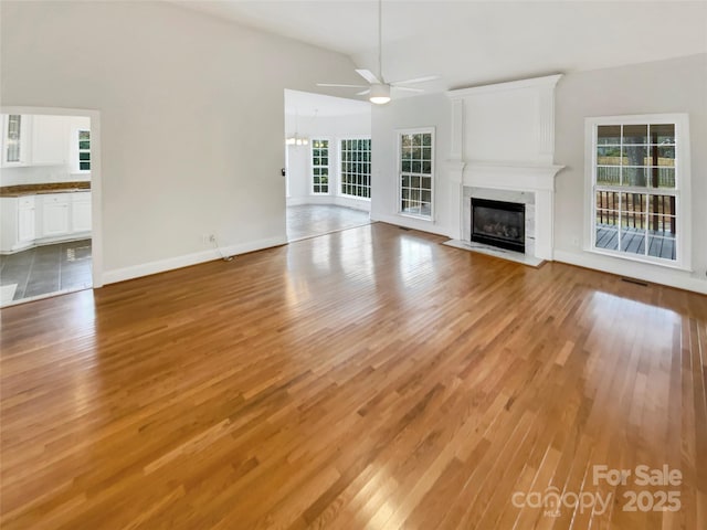 unfurnished living room featuring a premium fireplace, lofted ceiling, ceiling fan, and light wood-type flooring