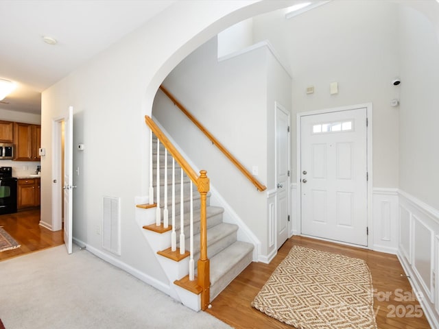 foyer with visible vents, stairway, a wainscoted wall, light wood-style flooring, and arched walkways