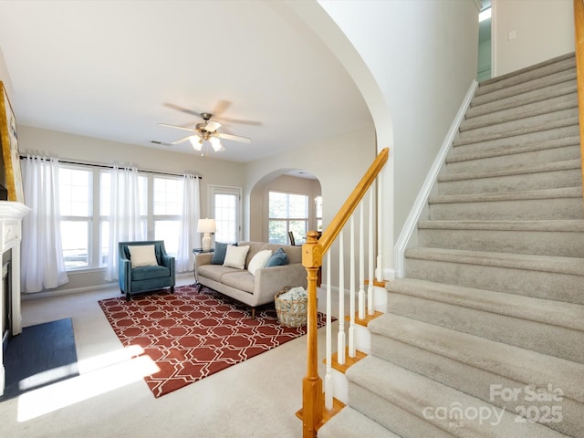 carpeted living area with visible vents, a fireplace, arched walkways, ceiling fan, and stairs