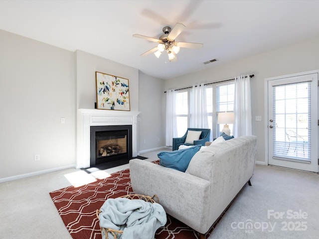 living area with visible vents, ceiling fan, baseboards, a fireplace with flush hearth, and light carpet