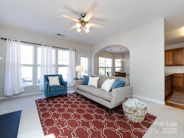 living area with visible vents, ceiling fan with notable chandelier, arched walkways, dark colored carpet, and baseboards