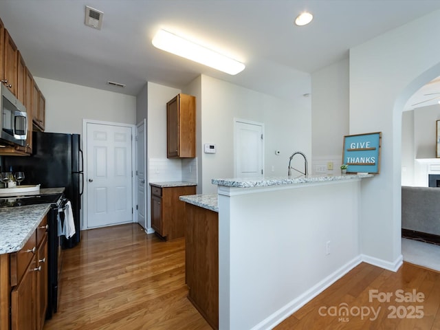 kitchen featuring wood finished floors, a peninsula, black range with electric cooktop, stainless steel microwave, and brown cabinets