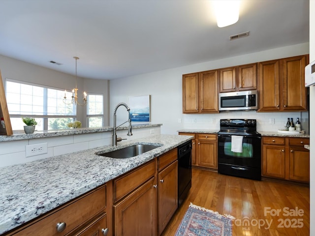 kitchen with visible vents, black appliances, a sink, brown cabinetry, and decorative backsplash