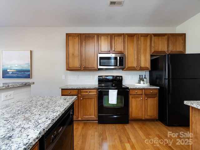 kitchen with light stone countertops, black appliances, light wood-style flooring, and brown cabinetry