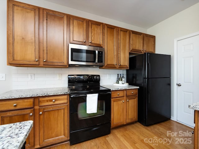 kitchen featuring black appliances, brown cabinetry, and light wood-style floors