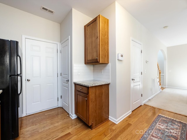 kitchen with brown cabinetry, visible vents, freestanding refrigerator, decorative backsplash, and light wood-type flooring