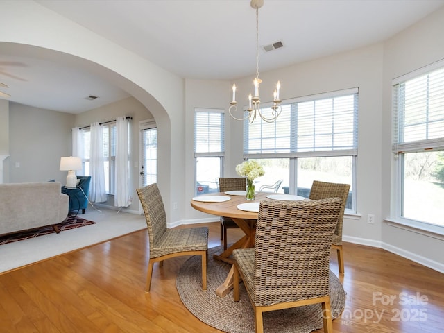 dining area with wood finished floors, visible vents, arched walkways, and a healthy amount of sunlight